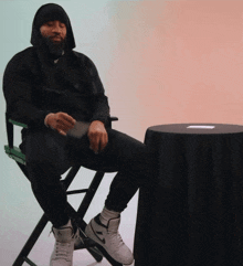 a man in a hooded jacket sits in a chair next to a table