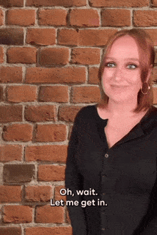 a woman is standing in front of a brick wall and says " oh wait let me get in "