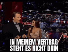 a man and a woman are standing on a stage with the words in meinem vertrag steht es nicht drin written above them .