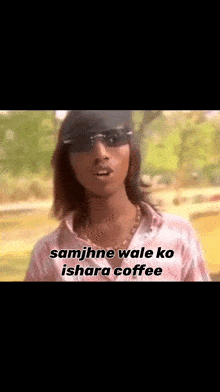 a man wearing sunglasses and a hat is standing in a park and talking .