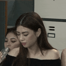 a woman is drinking water from a bottle while another woman leans on her shoulder