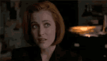a woman with red hair is wearing a black jacket and looking at the camera .