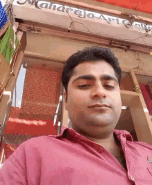 a man in a pink shirt is taking a selfie in front of a sign that says maharaja art gallery
