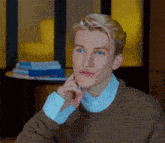 a young man with blonde hair and blue eyes is wearing a brown sweater and a blue striped shirt .