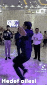 a man in a suit is jumping in the air while dancing in a room with other men .