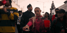 a group of people are walking down a street and one of them is holding a red cup