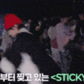 a man in a red hat is dancing in front of a crowd with the words stick in the corner .