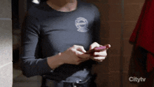 a woman in a black shirt is holding a cell phone in front of a citytv sign
