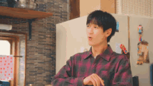 a young man in a plaid shirt is standing in a kitchen .