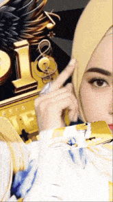 a woman wearing a hijab is pointing at something in front of a gold letter l