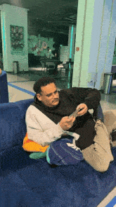 a man sits on a blue couch looking at his cell phone