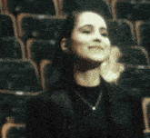 a woman wearing a black shirt and a necklace is sitting in a stadium applauding