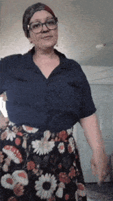 a woman wearing glasses and a blue shirt is standing in a room
