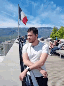 a man with a beard is leaning on a railing on a balcony with a flag in the background .