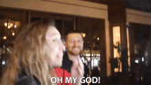 a man and a woman are standing in front of a building and the woman says oh my god