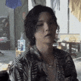a young man with long black hair is sitting in a room with a water bottle hanging on the wall .