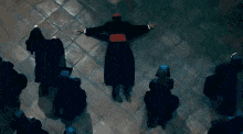 a group of people are standing around a priest laying on the ground .