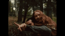 a man with a beard is carrying a woman in his arms in the woods .
