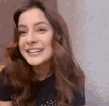 a woman with long brown hair is smiling and looking at the camera while wearing a black shirt .