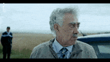 a man with gray hair and a mustache is standing in front of a police car