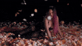 a woman with purple hair is laying on a pile of petals .