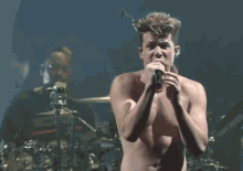 a shirtless man is singing into a microphone on stage