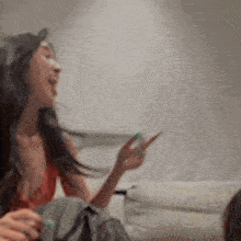 a woman is sitting on a couch talking on a cell phone while another woman looks on .