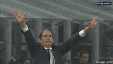 a man in a suit applauds in front of a cbs sports screen