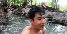a man without a shirt is standing in a stream of water .