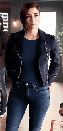 a woman is standing in a room wearing a blue jacket and jeans .