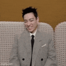 a man in a suit and tie is sitting on a couch smiling