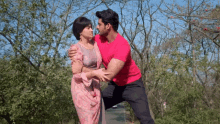 a man in a red shirt is holding a woman in a pink dress in a park .