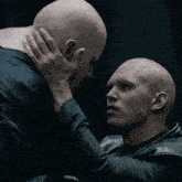two bald men looking at each other with one holding the other 's neck