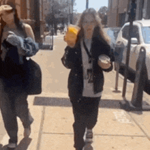 two women are walking down a sidewalk on a sunny day .