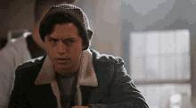 a young man wearing a beanie and a denim jacket looks at the camera