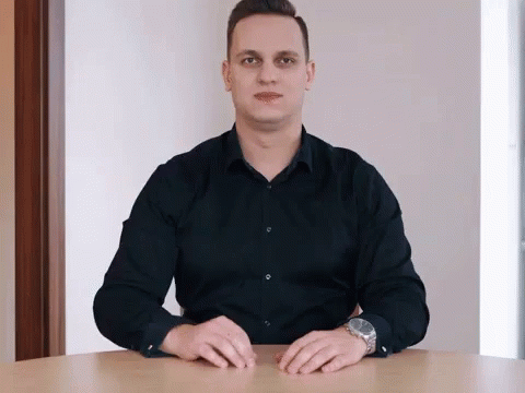 a man in a black shirt sits at a table with his hands on the table