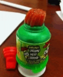 a green bottle with a red straw on top of it is on a wooden table .