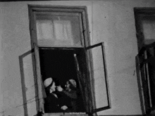 a black and white photo of a woman standing in a window .