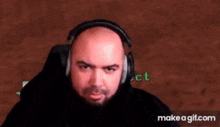 a bald man with a beard is wearing headphones and making a face .