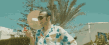 a man wearing sunglasses and a colorful shirt is standing in front of a palm tree .