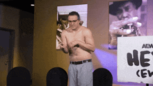 a shirtless man stands in front of a sign that says he 's