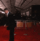 a man in a suit stands on a red carpet in front of a wall that says miscares and relief