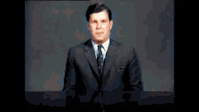a man in a suit and tie stands in front of a desk