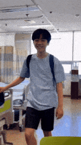 a young man wearing a blue shirt and black shorts is standing in a hospital room