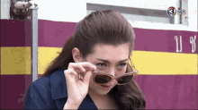 a woman wearing sunglasses is standing in front of a purple and yellow wall with the number 3 on it