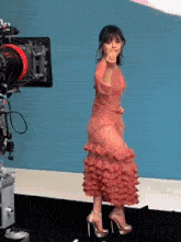 a woman in a pink dress is standing in front of a camera and giving a peace sign .