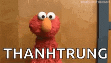 elmo from sesame street is standing in front of a wall with the words thanhtrung written on it .