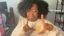 a woman wearing glasses and a white shirt with the letter b on it giving a peace sign