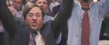 a group of men in suits and ties are raising their arms in the air in a crowd .