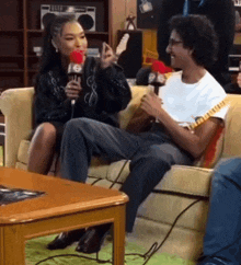 a woman is sitting on a couch talking into a microphone while a man plays guitar